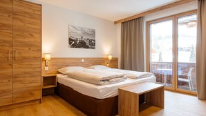 A modern bedroom with a wooden bed, a wooden wardrobe, a bedside table, and a large window with a view of the outdoors. - Studio Near the Slopes With Wellness Area (Mittersill)