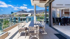 A balcony with a table and chairs, overlooking a cityscape and mountains.