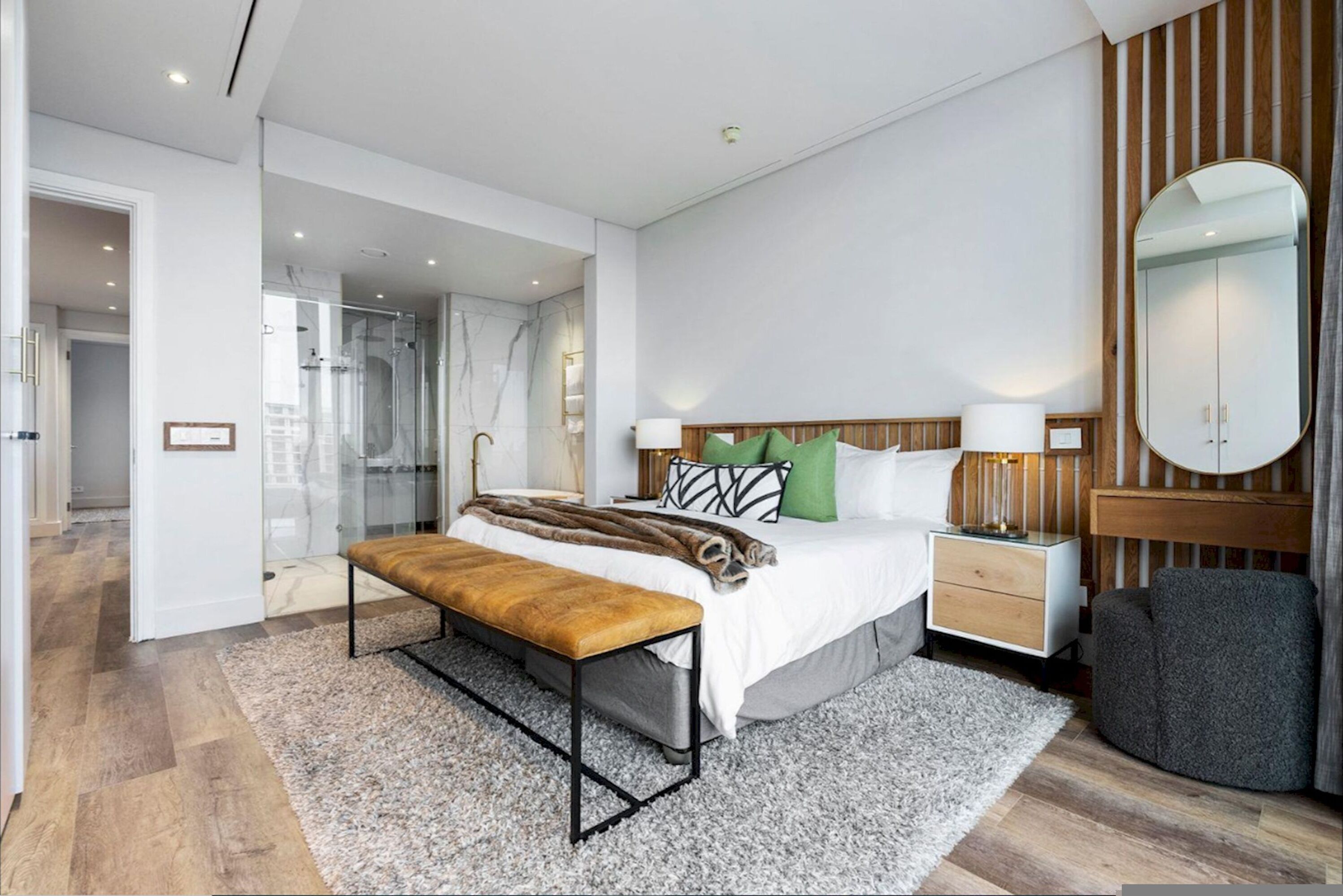 Un dormitorio moderno con una cama grande, un banco, una mesita de noche, un espejo y un vestidor.
