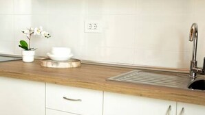 A kitchen with white cabinets, a wooden countertop, a stainless steel sink, and a small potted orchid.