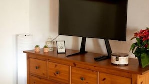 A wooden dresser with a flat-screen TV on top, a small plant, a framed picture, and a decorative item.
