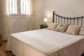 A bedroom with a bed, a nightstand, a lamp, and a window with curtains. - Elegante y Luminoso Piso Reci n Reformado (La Victoria de Acentejo)