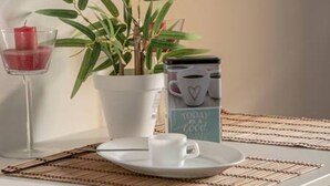 A table with a white cup and saucer, a glass with a red candle, a potted plant, and a canister with a heart design. - Elegante y Luminoso Piso Reci n Reformado (La Victoria de Acentejo)