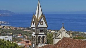 A coastal town with a prominent church featuring a tall spire and a smaller adjacent building with a tiled roof. - Elegante y Luminoso Piso Reci n Reformado (La Victoria de Acentejo)