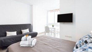 A modern hotel room with a grey sofa, a bed with a patterned duvet, a flat-screen TV mounted on the wall, and a ceiling fan. - Apartamento Brisa del Mar (Tacoronte)