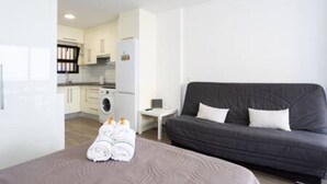 A modern hotel room with a grey sofa, a small bedside table, and a neatly made bed with towels. - Apartamento Brisa del Mar (Tacoronte)