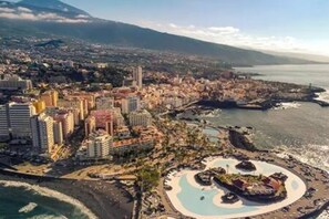 An aerial view of a coastal city with a prominent marina, high-rise buildings, and a large circular park area. - Apartamento Atardecer Martianez (Puerto de la Cruz)