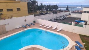 A swimming pool with lounge chairs, a view of the ocean, and a parking area. - Apartamento Atardecer Martianez (Puerto de la Cruz)