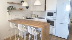 A modern kitchen with white cabinetry, a wooden island, white bar stools, pendant lights, and a built-in oven. - Apartamento Atardecer Martianez (Puerto de la Cruz)