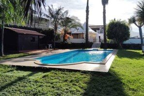 Ein Swimmingpool, umgeben von einer gepflegten Rasenfläche und Palmen, mit einem Haus im Hintergrund.
