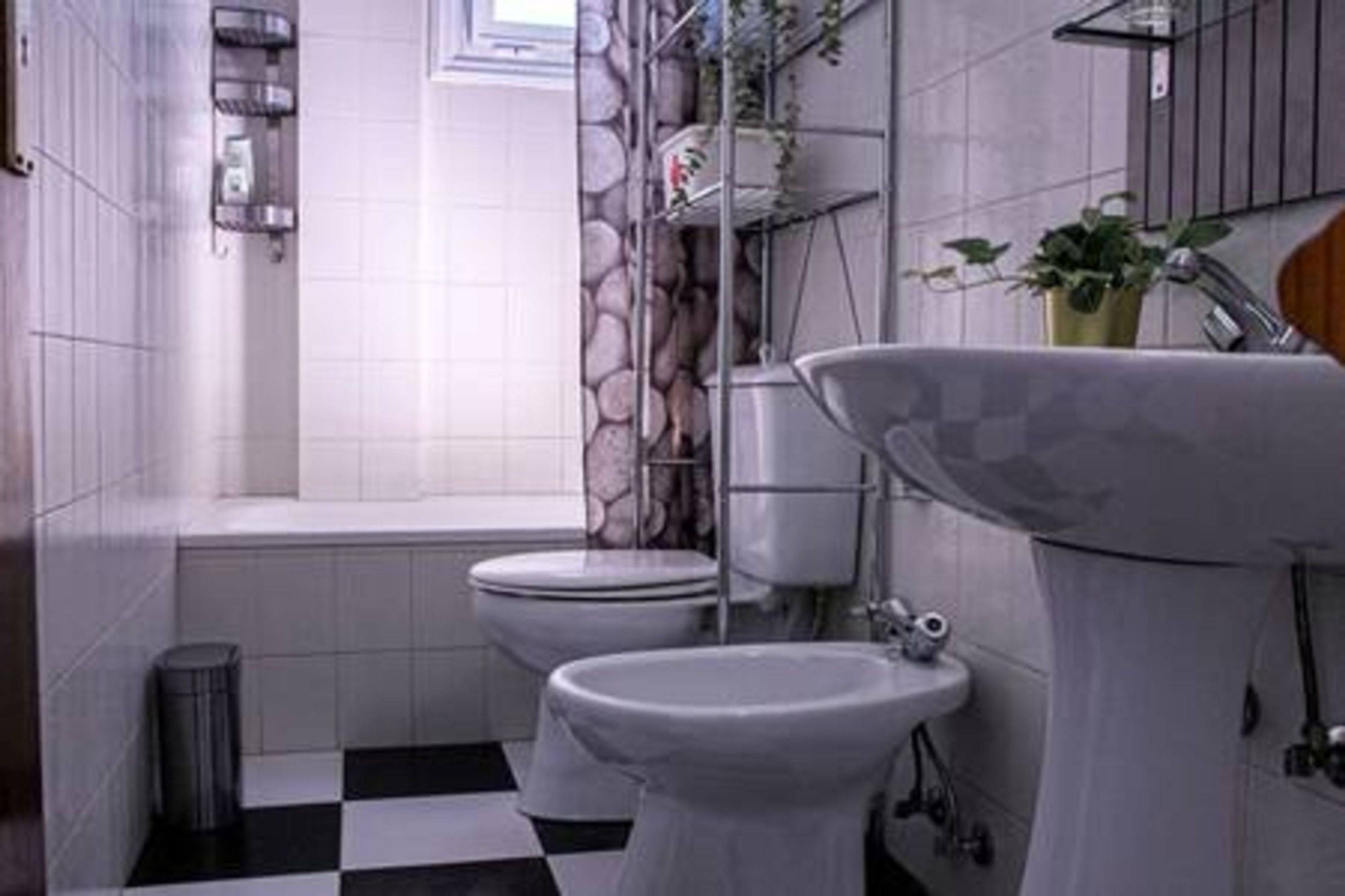 Un baño con dos inodoros, un lavabo, un cubo de basura y una ventana.