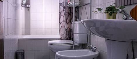 Un baño con dos inodoros, un lavabo, un cubo de basura y una ventana.