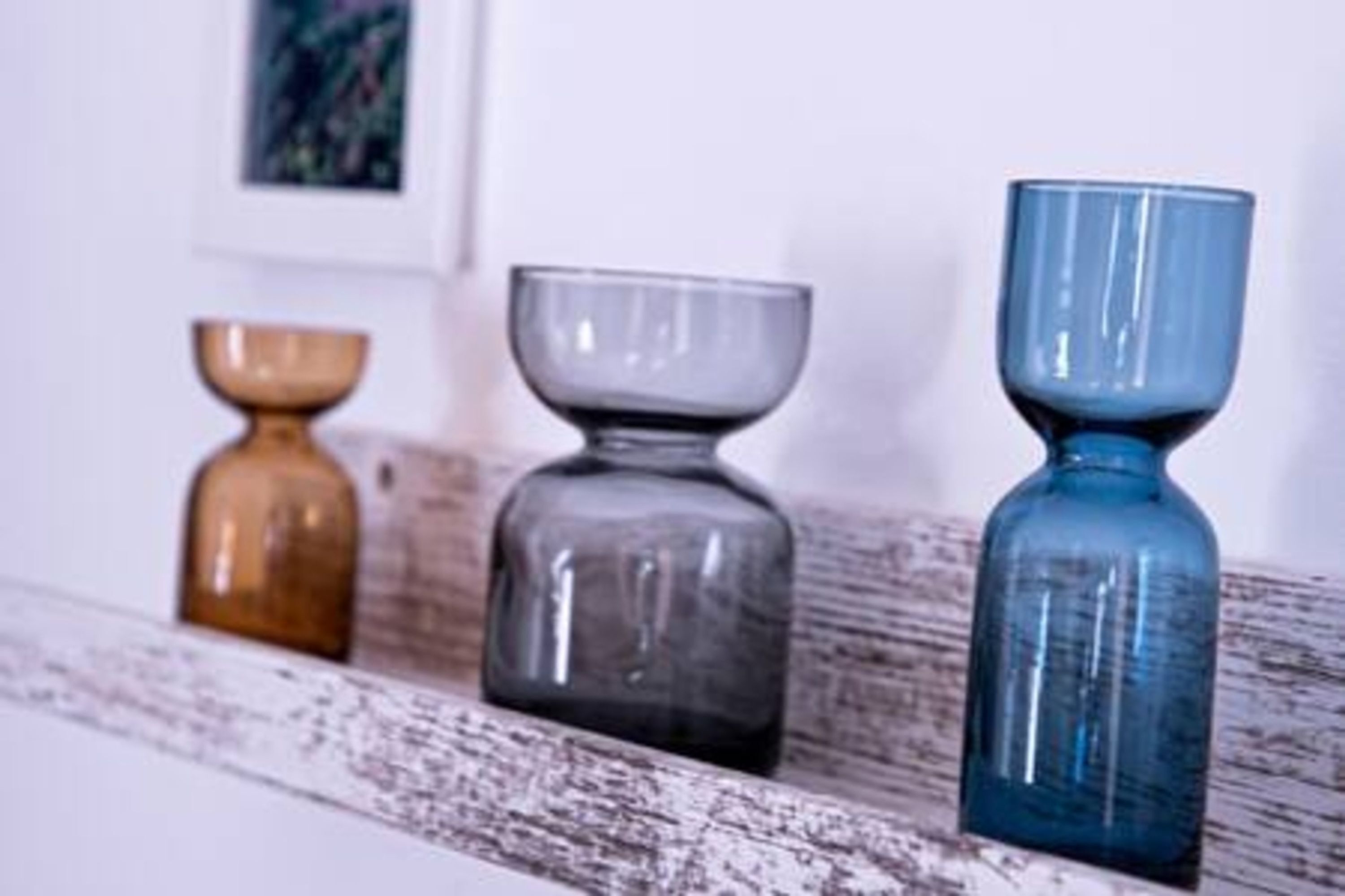 Three glass vases of different shapes and colors on a wooden shelf.
