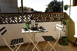 Un petit balcon avec une table et deux chaises, une plante en pot et une plante suspendue.