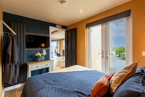 Une chambre à coucher avec un lit, une commode, un téléviseur et une vue sur l’extérieur.