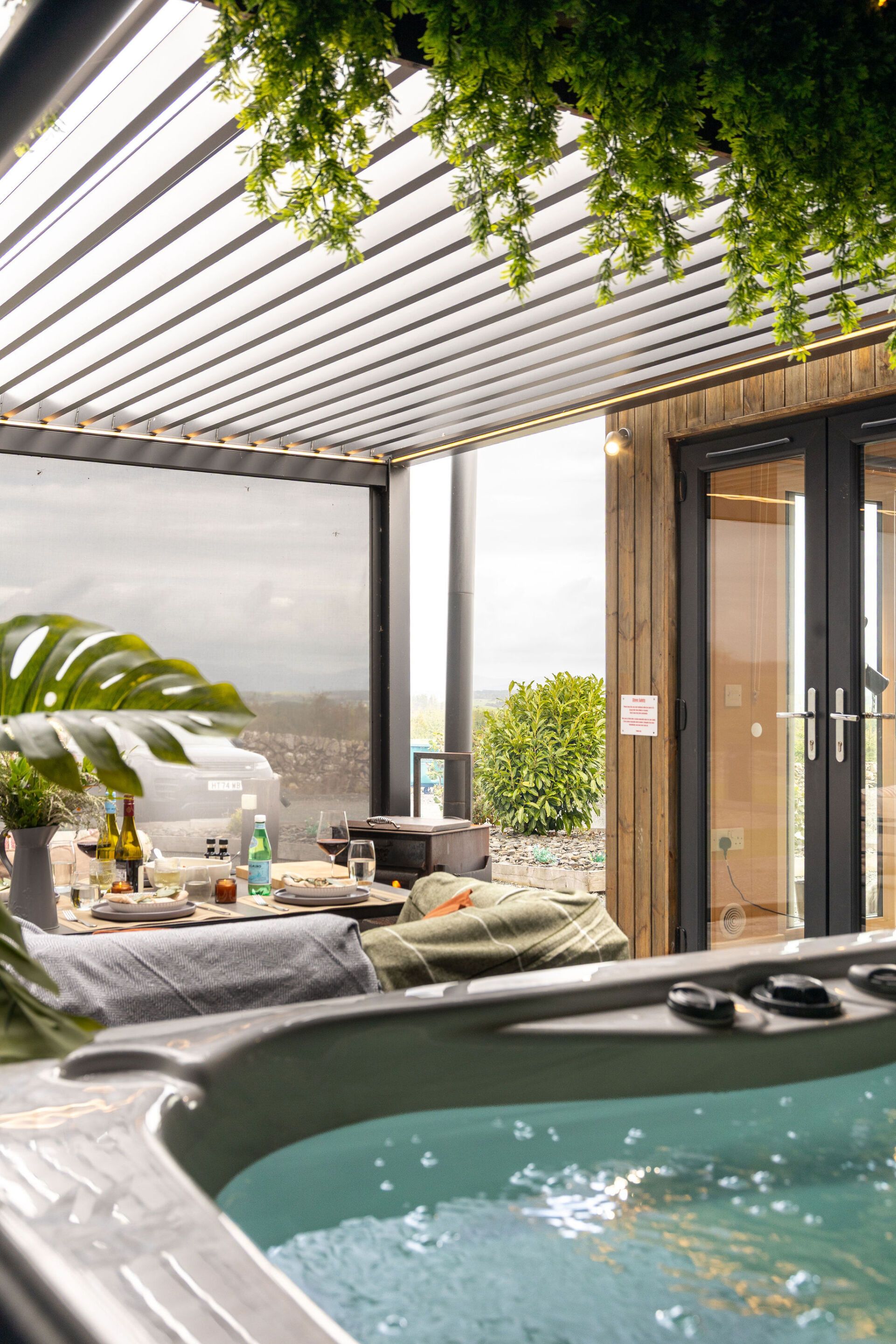 A hot tub area with a view of the landscape, a wooden door, and a table with drinks and glasses.