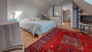 Un dormitorio con cama, cómoda, televisor y una alfombra roja estampada.