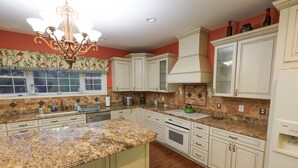 A kitchen with granite countertops, white cabinetry, a chandelier, and a window with decorative curtains.