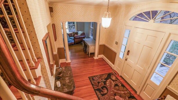 A staircase leading to a living area with a wooden floor, a dining table, and a patterned rug.