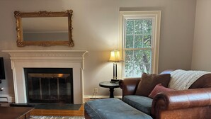 A living room with a fireplace, leather sofa, ottoman, patterned rug, and a large mirror.