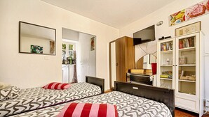 Een hotelkamer met twee bedden, een kledingkast, een televisie en een boekenkast.