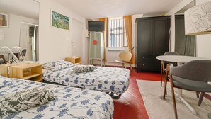 Een slaapkamer met twee bedden, een bureau, een stoel, een televisie en een deur.