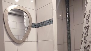Een badkamer met witte tegels, een ronde spiegel, een wastafel en een douchegedeelte met gordijnen met een vlindermotief.
