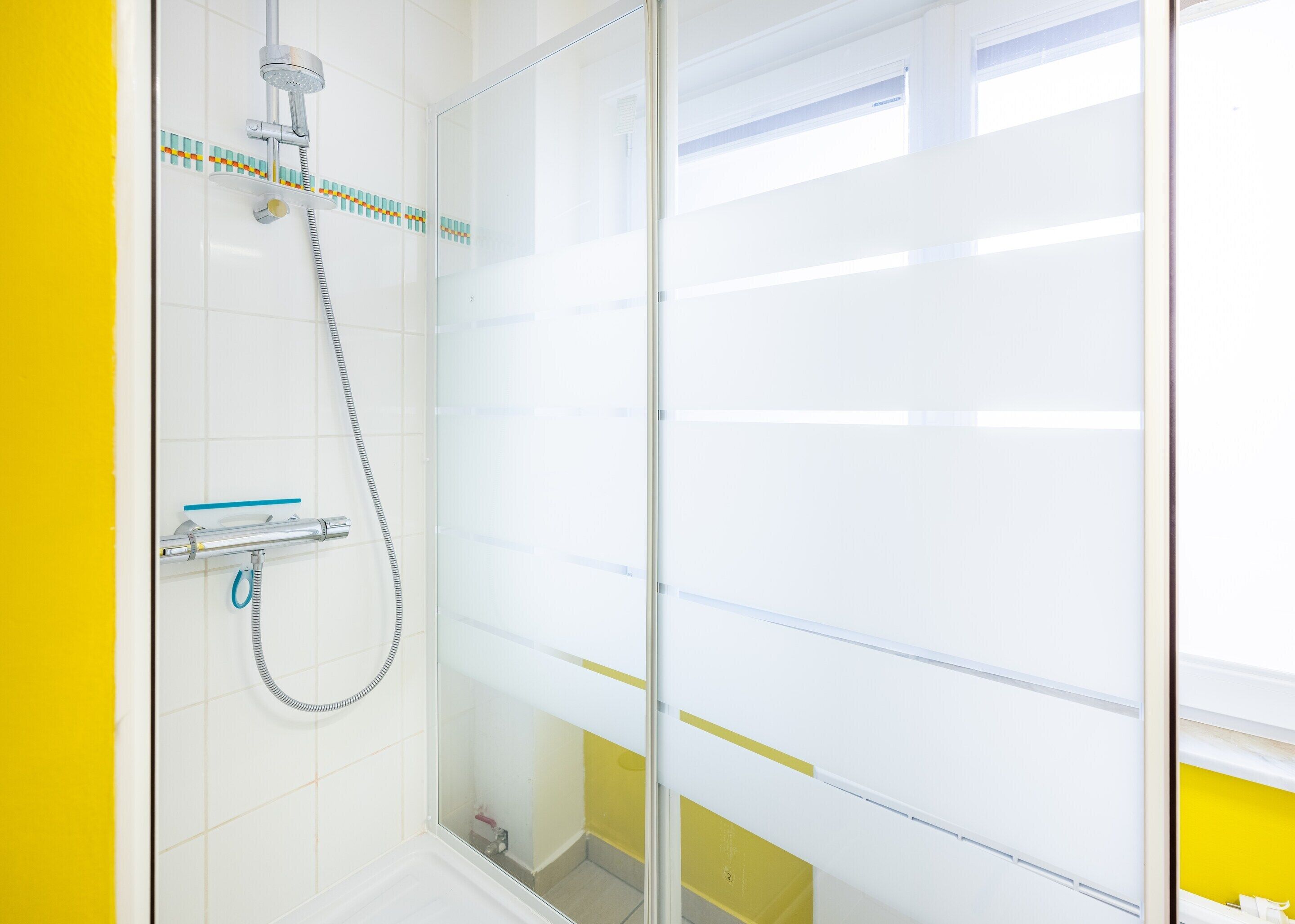 Ein modernes Badezimmer mit Duschkabine aus Glas, weiß geflieste Wände und einer gelben Akzentwand.