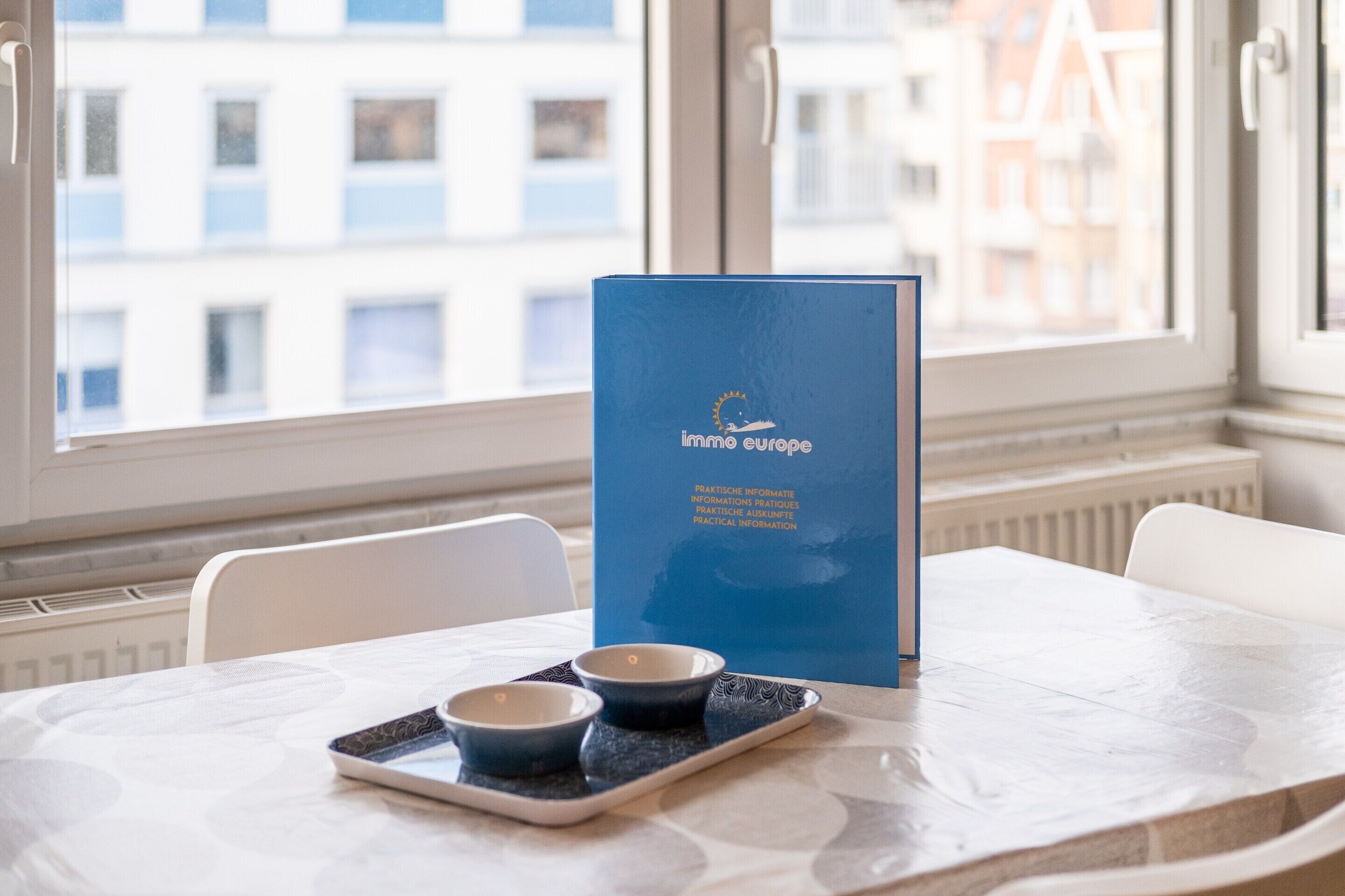 A table with a blue menu stand, two bowls, and a tray in a room with a window view.