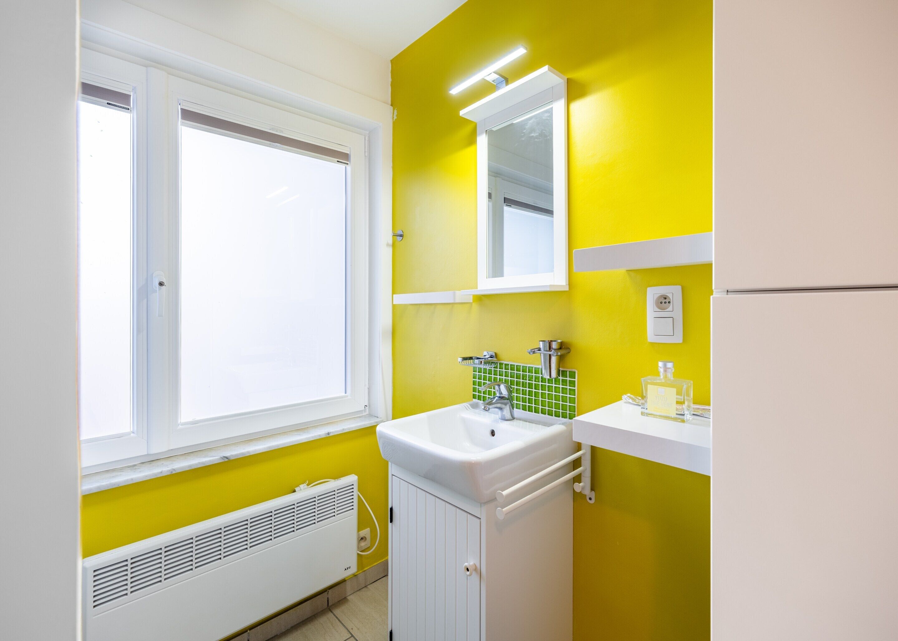 A bathroom with a window, white sink, and yellow walls.