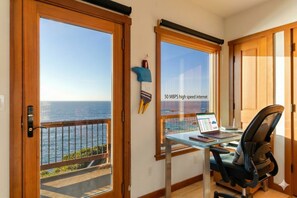 A room with a desk, chair, and a view of the ocean.