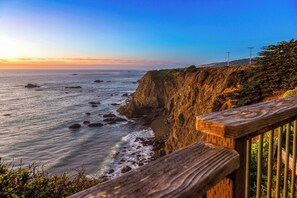 A coastal landscape with a wooden railing, rocky cliffs, and a clear sky.