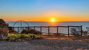 A sunset view from a coastal property with a wooden fence, a metal gate, and a rocky foreground.
