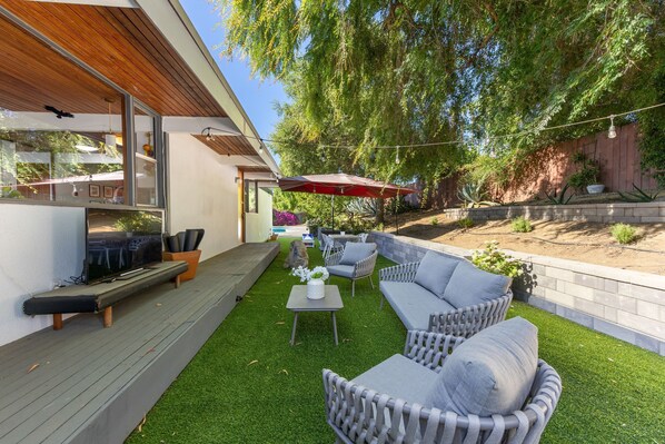 Une terrasse extérieure moderne, dotée d’une plateforme en bois, d’un téléviseur encastré et de mobilier d’extérieur.