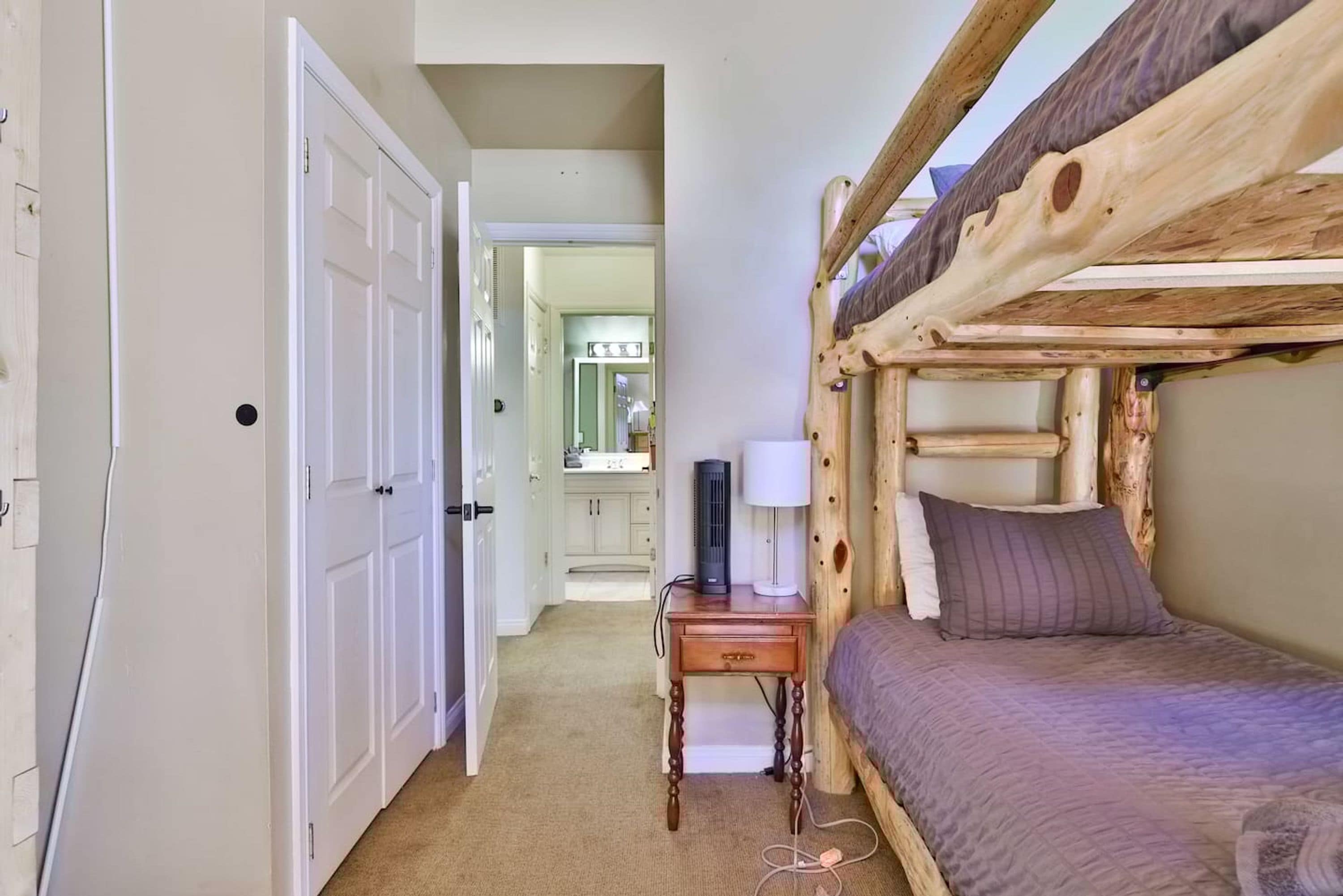 A room with a bunk bed, a desk with a lamp, and a door leading to a hallway.