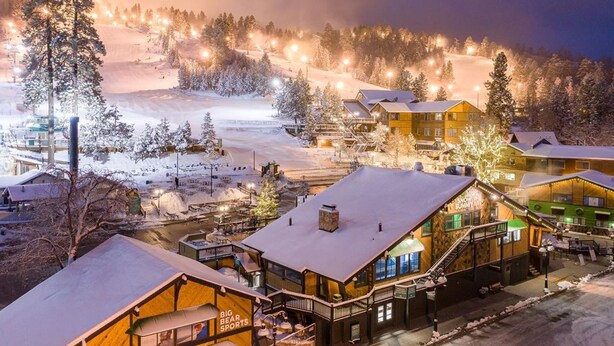 Una cabaña nevada con una pista de esquí al fondo.