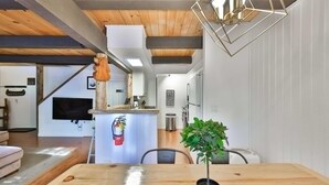 Una cocina moderna con techo de madera, un comedor con mesa de madera y una planta en maceta.