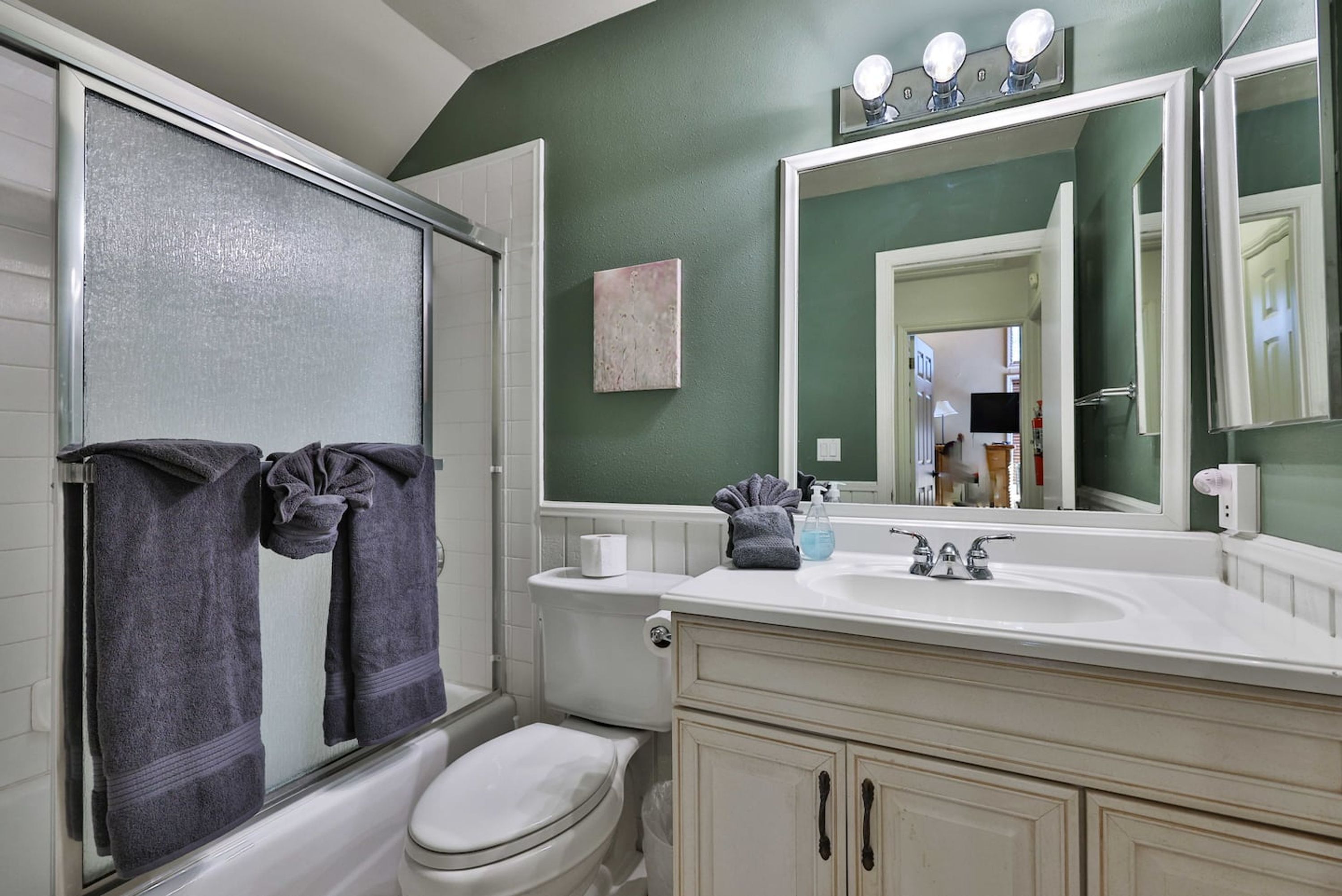 A bathroom with a shower, toilet, vanity, and a large mirror.