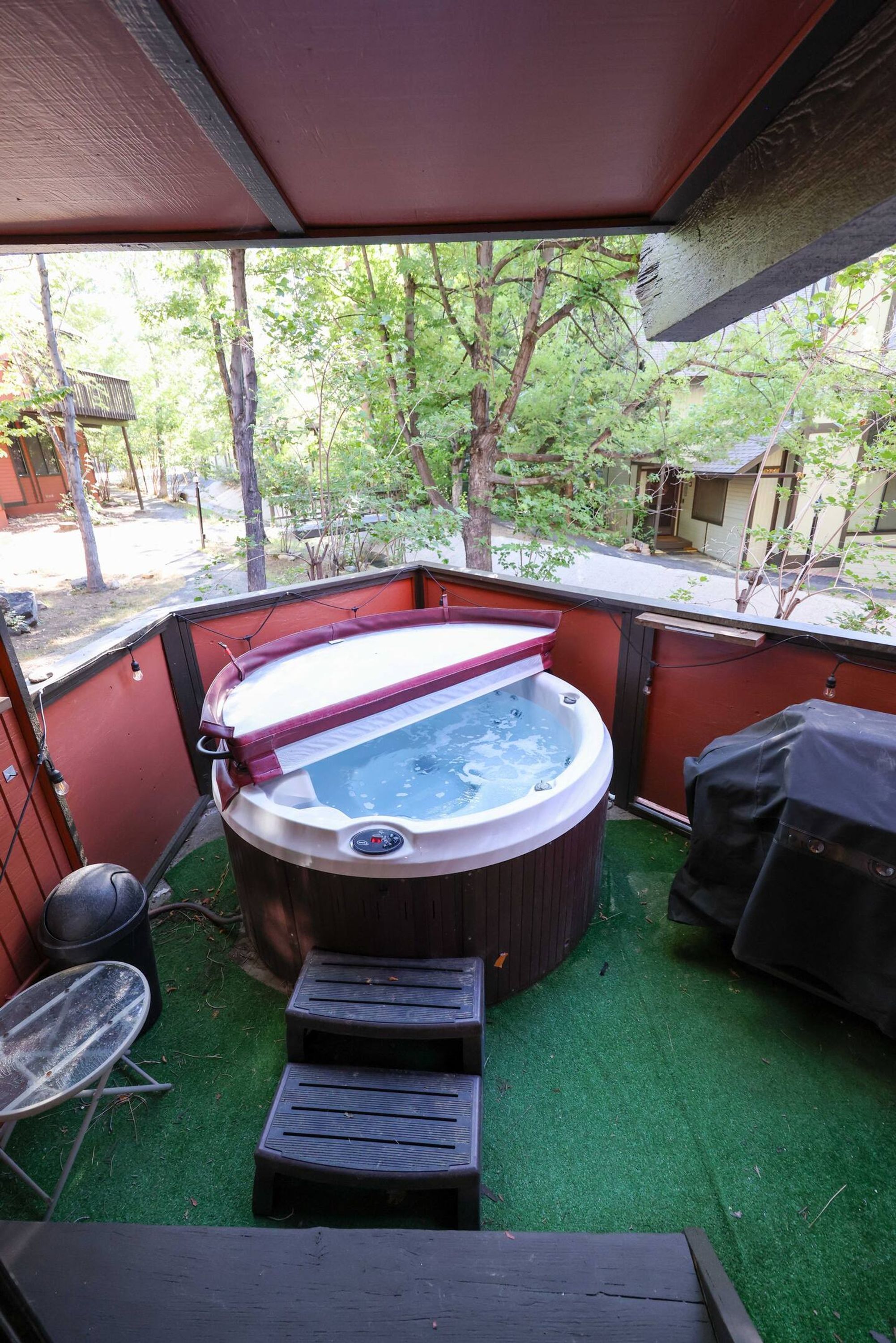A hot tub with steps, a covered patio, and a view of a wooded area.
