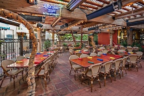 An outdoor dining area with wooden tables and wicker chairs, surrounded by a rustic wooden ceiling and brick flooring. - Pool and Gym Access Luxury Condo (San Diego)