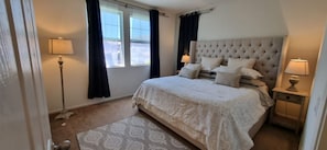 A bedroom with a large bed, two bedside lamps, a window with curtains, and a patterned rug. - Pool and Gym Access Luxury Condo (San Diego)