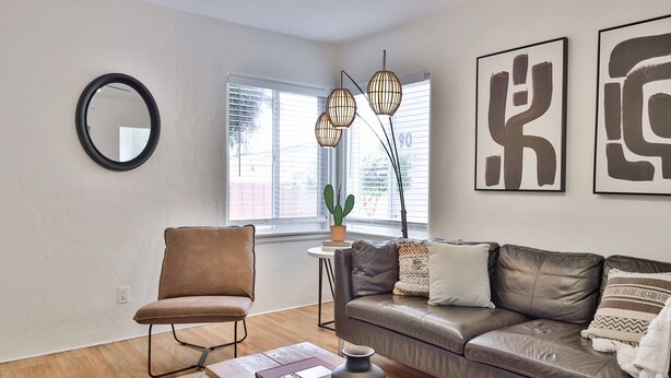A living room with a brown leather sofa, a brown leather chair, a round mirror, and abstract art on the wall. - Normal Heights Hideaway (San Diego)