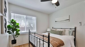 A bedroom with a bed, a ceiling fan, a window with blinds, and a potted plant. - Normal Heights Hideaway (San Diego)