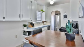 A modern kitchen with white cabinets, a wooden dining table, and a potted plant. - Normal Heights Hideaway (San Diego)