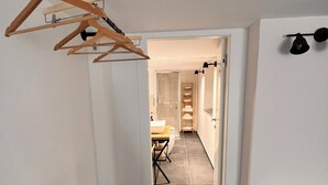 A narrow hallway with a wooden hanger rack, a black chair, and a white bench. A glass door leads to a bathroom with a toilet and sink. - Charming 2-bedroom house in lovely Catania with WiFi, AC (Catania)