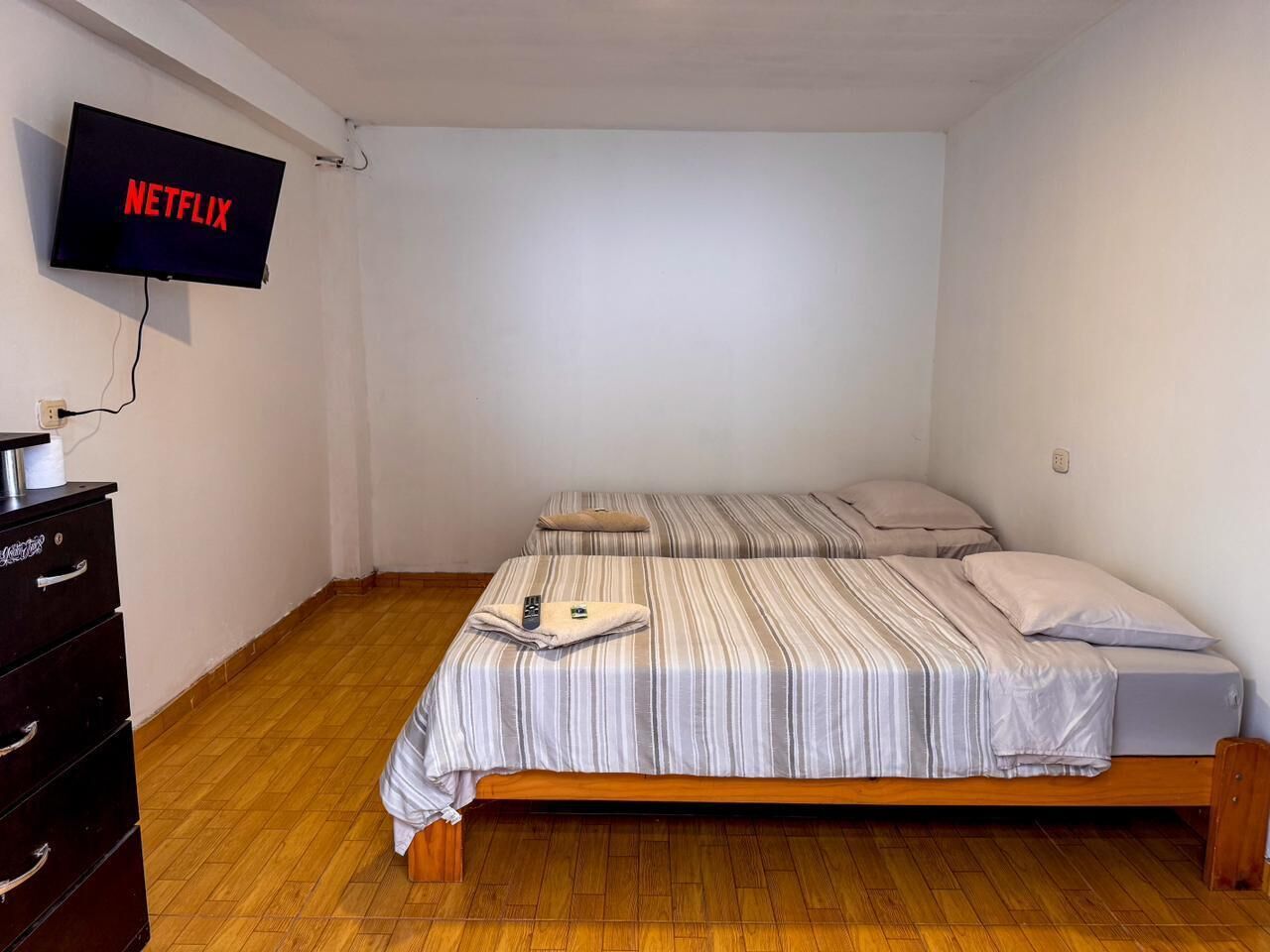 A small, clean room with two beds, a TV mounted on the wall, and a wooden dresser.