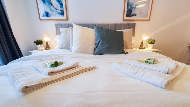 A neatly made bed with white linens, two pillows, and two bedside tables with lamps and small potted plants. - Lovely Flat in Kiln Close With Free Parking (Gloucester)