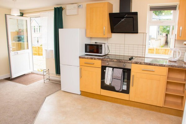 A compact kitchen with wooden cabinets, a microwave, an oven, and a refrigerator.