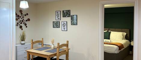 Una habitación con una mesa de comedor y sillas, una cama con almohadas, y una pared con cuadros enmarcados.