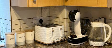 Una cocina con armarios de madera, un tostador blanco, una cafetera y dos recipientes etiquetados como 'café' y 'té'.